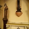 Statues of St. Teresa Of Lisieux and St. John of the Cross inside Carmelite Church. The statue of St. John of the Cross is mounted on the wall. He is wearing a black clerical robe and beige cape. He is crossing his arms, with a small cross held by his left hand. A disk-like halo with floral patterns is behind his head. St. Teresa stands on a brown wood-like pedestal. She wears brown clothing with a beige cloak. She is hugging a cross with pink flowers growing on it. Also in this picture is an altar-like table with a Celtic cross in front under the statue of St. John. St. Theresa's podium stands on the left of this table.