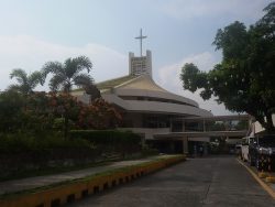 The Christ the King Parish in Greenmeadows, Quezon City, has the appearance of two white concrete slightly-thickened discs formed by the ceiling and the external veranda. There's a gap between the discs through which you can see the wall and the glass doors. On top of the upper disc is a green conical roof with a hollow rectangular structure on top; a cross is mounted on top of this structure. A bridge is also seen in this picture connecting the church to a building across the driveway.