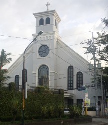 The church building of Christ the King Parish as seen from along Bansalangin St. north of Calumpit St. The frontage is mostly white with five half-oblong and one circular glass windows.