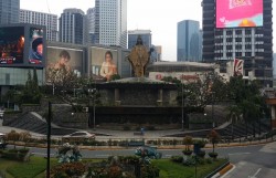 The external structure of the Shrine of Mary, Queen of Peace as seen from one of the footbridges connecting the four corners of EDSA-Ortigas Avenue intersection. The external structure is surrounded by elevated platforms with staircases and ramps on the opposite sides. The elevated platforms and part of the staircases have plants. The doors to inside the church are under the staircases. The bottom-center of the structure has murals depicting the events of EDSA II. The front-center of the structure has metallic letters of the Bible verse from 2 Chronicles 7:14, although it only shows Chronicles 7:14 (the 2 probably fell-off or something). At the top is the iconic golden brown statue of the Blessed Virgin Mary wearing a crown and exposed Immaculate Heart and with birds on her left hand and right shoulder. At the background is the Robinsons Galleria and several buildings in the Ortigas Business District.