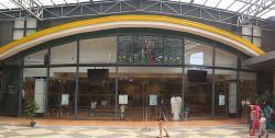The Chapel of the Holy Family has a facade of mostly transparent glasses, arches of yellow and white stripes above the glasses, and a dark gray concrete wall on the sides and above the arches. Two large windows, each with four divisions, are found on the sides above the arches. Below the arches are seven glass panels, six of which are transparent, and the one at the center shows a depiction of the Holy Family in a field of flowers and grasses. Below these glass panels are larger rectangular glass panels through which you can see the inside of the chapel. The second and fifth lower glass panels are smaller glass doors, while the lower glass panel in the middle below the depiction of the Holy Family is the main entrance.