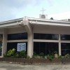 The structure of Holy Family Parish is like a large bungalow and semicircle when viewed on top. It has a small cross and a taller building at the back. It is predominantly white but has black grill windows and gates.