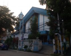 The Immaculate Conception Parish is on an elevated ground, with the elevation starting on its gates. The church has a triangular roof and a smaller bell tower with a pyramidal roof and with a cross on top. The church structure is mostly white with blue on the roof, near the windows, and the protrusion above the main entrance.