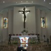 The altar and sanctuary. The altar is covered with white cloth and has stained glass design on its base. Above the altar is the crucifix mounted on the wall and illuminated from the back. On the sides of the crucifix are two stained glass: the one on left depicts Mary while the one on right depicts Joseph and child Jesus (or maybe another saint with a boy).