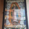 An icon of Our Lady of Guadalupe situated on the external wall of OLPH Parish in Cubao. It depicts Mary in white clothing with a blue-green cloak. Several stars are printed all over the cloak. Mary's hands are in Amen position. She is surrounded by clouds, and the clouds are surrounded by margins decorated by leaves and white flowers. The image is inside a glass panel that has joints and lock; looks like it can be opened. The text on top says Our Lady of Guadalupe, while the one at the bottom is Pamayanan ng Guadalupe, a Filipino phrase which means Community of Guadalupe.
