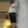 A statue of St. Pedro Calungsod in white long sleeves shirt, black pants, and slippers, is hugging a large feather while holding a book with both hands. The statue is on a wooden platform attached to a cylindrical pillar of the chapel.