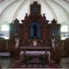 The sanctuary of San Diego is mostly brown tabernacle and altar in front of a white wall. The altar at the center has white cloth on it but is otherwise pinkish with a brown pattern. The wooden structure at the back has statues of saints: the one at the center is the biggest and the ones on the sides are slightly smaller. The back of the saints has blue and white sky-like design wallpaper or paint. Under the biggest saint statue is the tabernacle, a gold or bronze box. There are statues of angels on the sides of the tabernacle, just in front of the smaller statues of saints. There is also a brown lectern on the left (right if you are facing the nave) and the floor has a design of brown and white chequers.