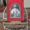Sacred Heart image in San Pedro Bautista Parish A grayscale image of Jesus showing his sacred heart inside a frame, which is on an iron stand. The stand has a semicircular arch on which the frame can lean. The grayscale image is semi-oblong with the round part above Jesus' head. The grayscale image is surrounded by goldtone border, which is on a red background that occupies the rest of the frame.