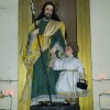 Joseph with young Jesus Statue of Joseph with staff on the one hand and holding the hand of child Jesus with the other. The other hand of Jesus is holding a black toolbox. The staff has flower near the top. Both Jesus and Joseph have halos on the back. Joseph wears mostly green and yellow while Jesus wears white. They are both enclosed by gold or bronze-colored arch.