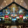 The sanctuary of Sto. Niño De Congreso Parish has a white triangular ceiling with small circular lights. The sanctuary is dominated by a glass pane depicting Jesus in white and with his arms spread in what looks like Heaven. Two angels are kneeling and blowing trumpets in front of him. A cross is also visible on his back, which is a hole in the glass pane. The right side of the panel (as seen from the nave) depicts the Our Lady of La Salette apparition of Mary with three different poses: weeping, blessing children, and with arms cross. On the left side is an image of the Sto. Niño, a depiction of child Jesus in a red kingly outfit and holding an orb. Goldtone statues of Sto. Niño and Our Lady of La Sallete are below the glass pane, below their corresponding depictions on the glass pane. Between the goldtone statues in the Sun-like tabernacle surrounded by four smaller statues of angels, each holding a trumpet: two on each side. In front of the tabernacle is a white altar, with a white cloth on top and an illuminated depiction of a lamb holding a red cross flag. Two lecterns are also seen here: the one on the left is larger and has characters alpha and omega, while the one on the right is smaller and has letters JHS.