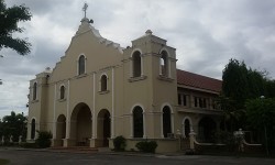 The external structure of St. Jude Thaddeus Parish is mostly beige with white highlights along the edges of its windows and facade. Its facade is flanked by two towers and has a cross on top. The windows and the entrance are all semi-oblong. The color of the roof, which is visible on the side, is maroon.