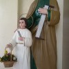 Two statues, that of Jesus as a child with Joseph. Joseph is wearing a green robe and a brown cloak over it. His left hand is holding a saw, while his right hand is holding the right shoulder of Jesus. Jesus is wearing a white robe. His left hand is holding what looks like a paper, and his right hand is holding a basket full of flowers.